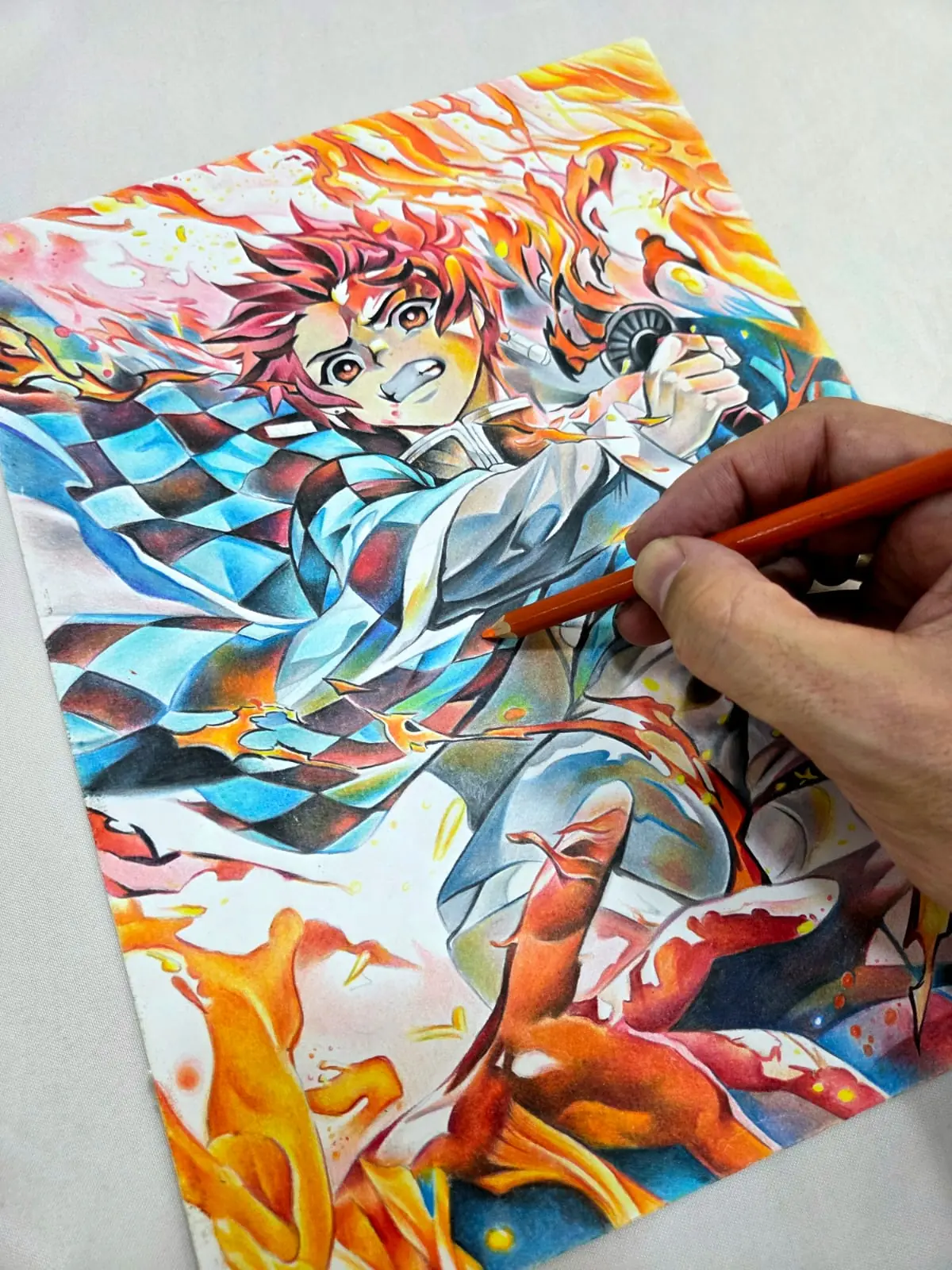 Tanjiro a lápis de cor, de haori xadrez azul entre chamas laranja, com uma mão segurando o lápis sobre o papel